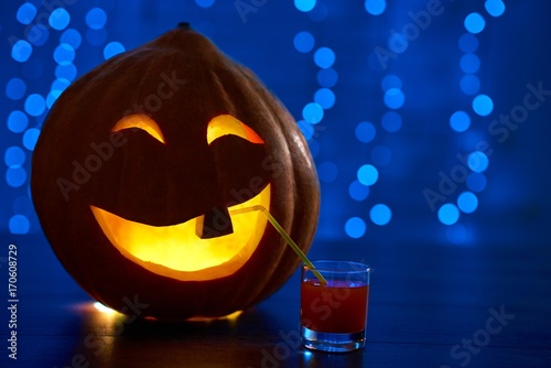 Sticker Close up of red smiling pumpkin with one tooth and big eyes, decoration prepared for Halloween smiling and drinking cocktail at party