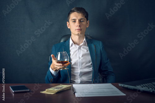 Man in suit sitting in chair. Boss drink alcohol in the glass and enjoys the success. Concept of a successful business