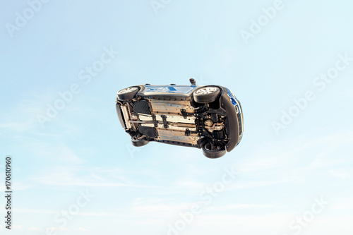 A car flying through the air (in the pale blue sky) with the underside including, wheels, engine and exhaust pipe visible.