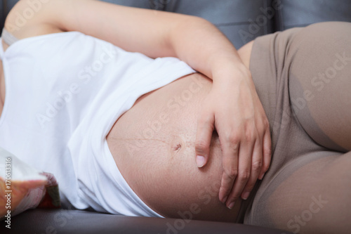 Pregnant woman putting hand on the belly while sleeping on sofa