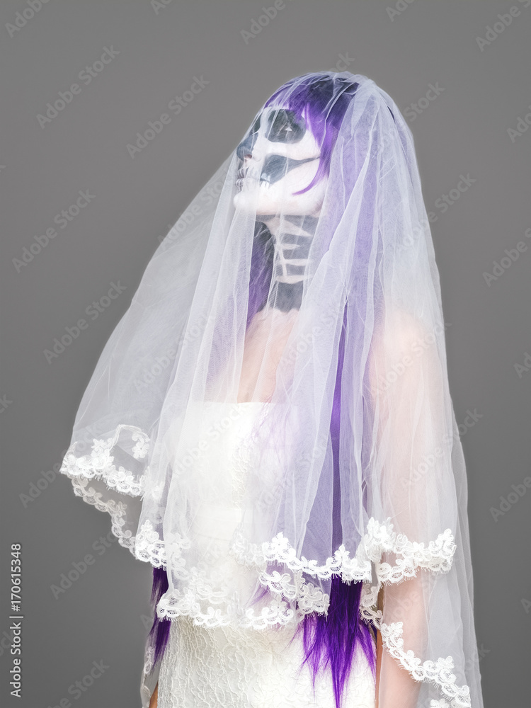 Portrait of woman looks upwards with terrifying halloween skeleton makeup and purple wig bridal veil, wedding dress over gray background. Black wedding Portrait of woman looks upwards with terrifying halloween skeleton makeup and purple wig bridal veil, wedding dress over gray background. Black wedding