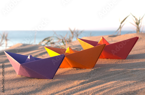 Three paper boats on a beach  Purple  orange and red