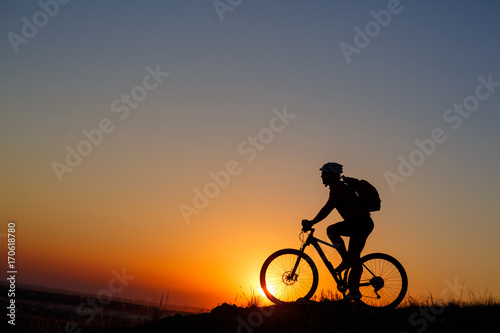 Silhouette of a bike tourist on mountain peak.