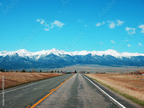 Empty road in Colorado countryside in USA on a sunny day with bright blue sky and snow mountain background