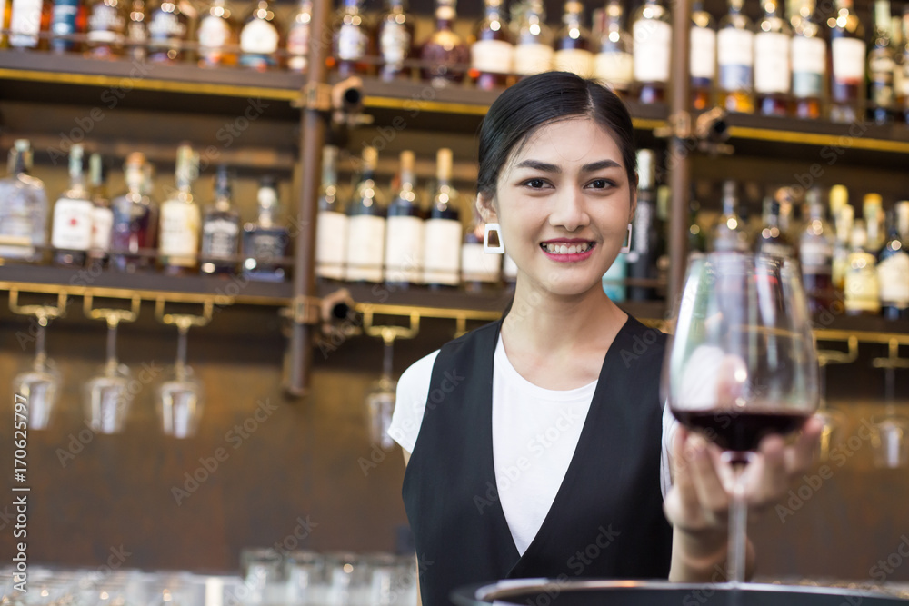 Young Asian Woman Waiter Restaurant Catering Service Happy Emotion. Woman Waiter Present Red-Wine for Customer at Bar. Woman with Wine in Bar Concept.