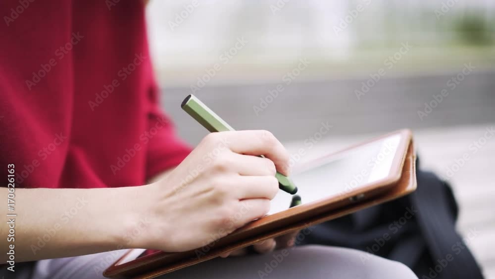 Close up of hands of an unrecognizable young woman wearing a red sweater working at her tablet computer with a special pen. Locked down real time close up shot Close up of hands of an unrecognizable young woman wearing a red sweater working at her tablet computer with a special pen. Locked down real time close up shot