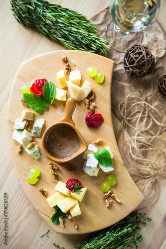 Close-up of a cheese plate. 4 types of cheese, soft white brie cheese, camembert, semi-soft briques, blue, roquefort, hard cheese. Walnuts, green grapes, sauce, white wine. Beautiful serve, top view