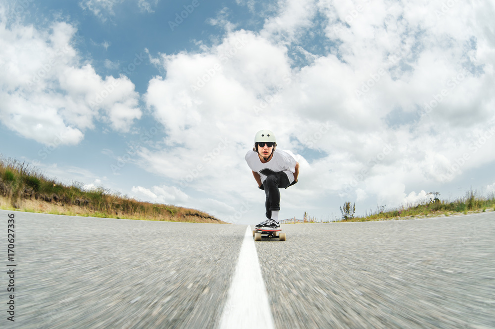 A guy wearing a helmet and sunglasses is riding his longboard on a country road