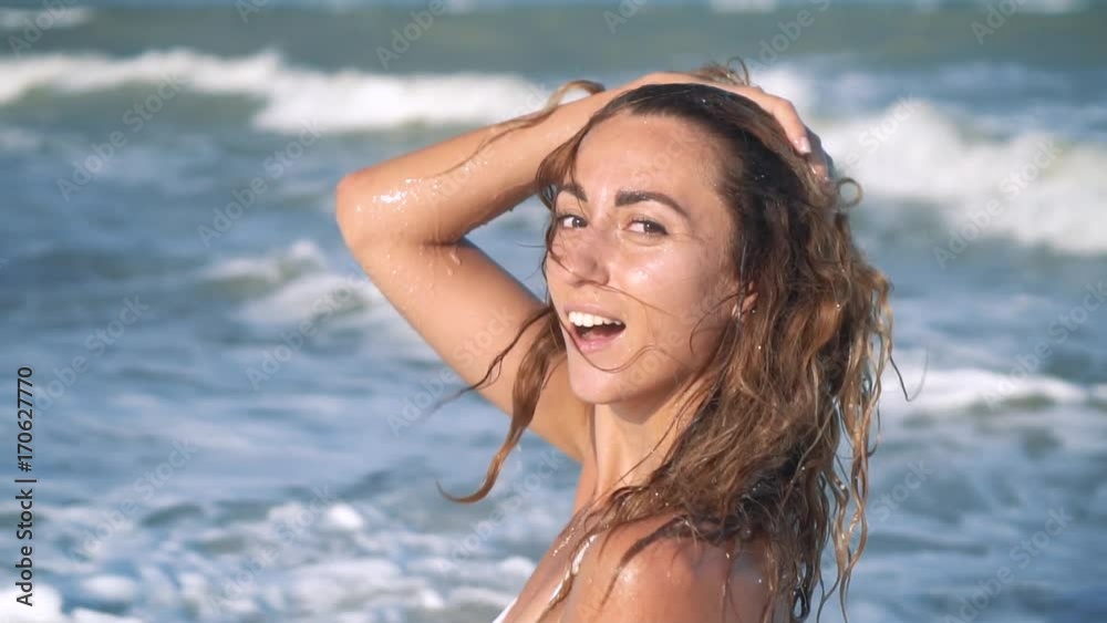 Young beautiful sexy tanned girl in bikini with curly hair sitting on the beach at sunset by the sea. She smiled enigmatically, stroked herself and. Slow motion. 120fps Young beautiful sexy tanned girl in bikini with curly hair sitting on the beach at sunset by the sea. She smiled enigmatically, stroked herself and. Slow motion. 120fps