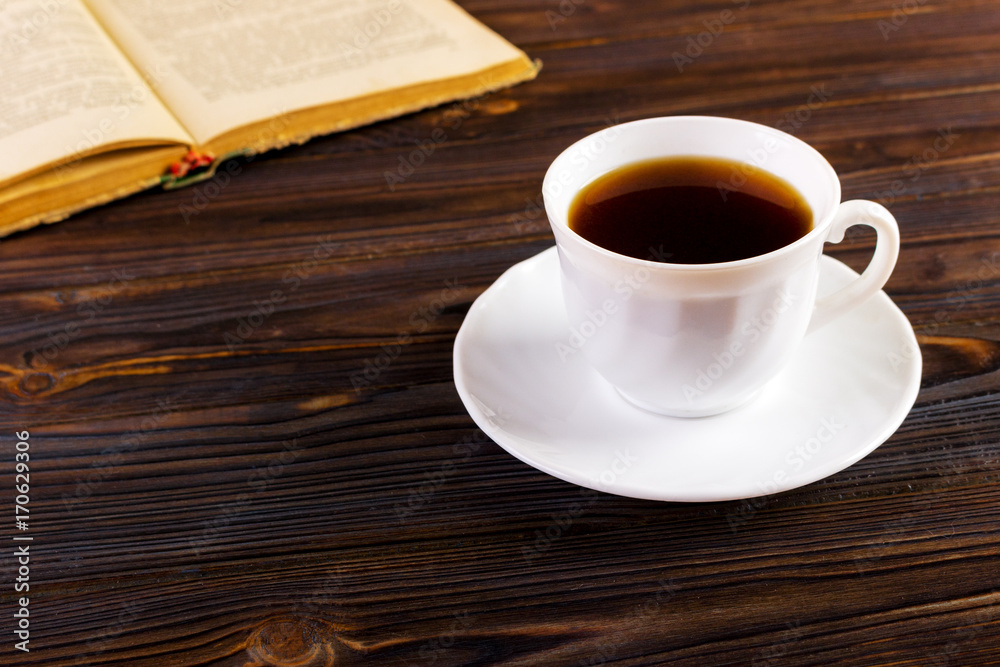 old book and a cup of coffee on a wooden background, toned image old book and a cup of coffee on a wooden background, toned image