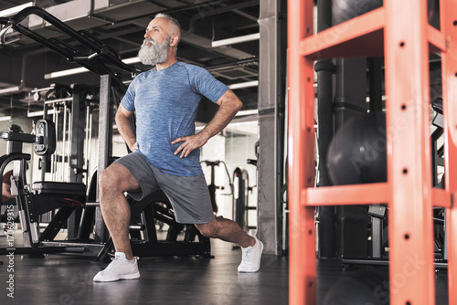 Stylish old male is enjoying workout in modern gym