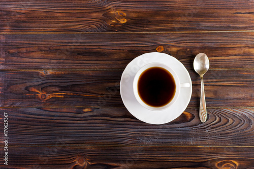 White Cup with coffee on a platter and spoon on wooden background