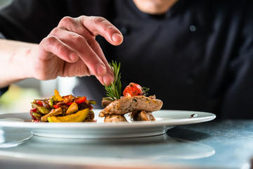 Chef finishing and garnishing food he prepared, a dish with pork meat and vegetables