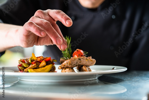 Chef finishing and garnishing food he prepared, a dish with pork meat and vegetables