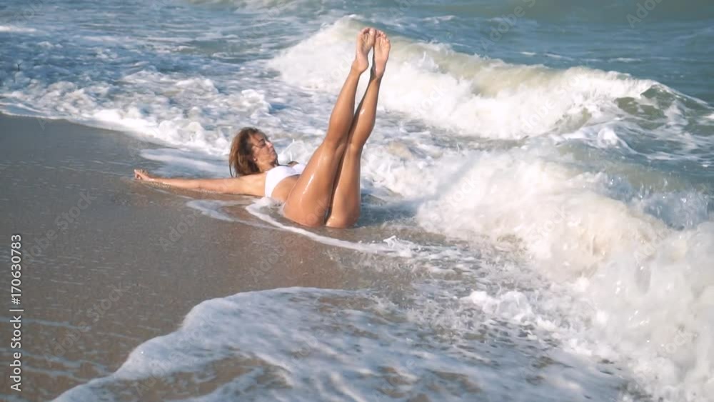 Young beautiful sexy tanned girl in bikini with curly hair sitting on the beach at sunset by the sea. She smiled enigmatically, stroked herself and. Slow motion. 120fps Young beautiful sexy tanned girl in bikini with curly hair sitting on the beach at sunset by the sea. She smiled enigmatically, stroked herself and. Slow motion. 120fps
