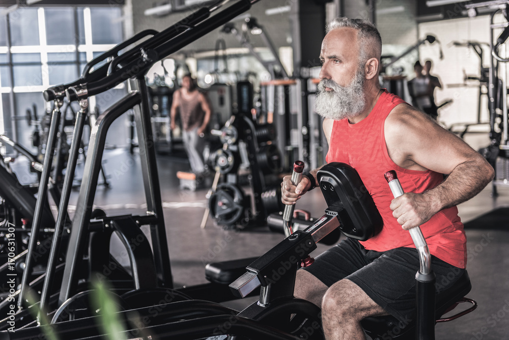 Pleasant senior male is having intensive workout in athletic center Pleasant senior male is having intensive workout in athletic center