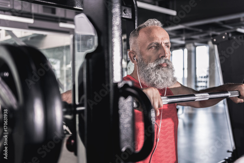 Pensive serious male with beard enjoying workout in athletic center