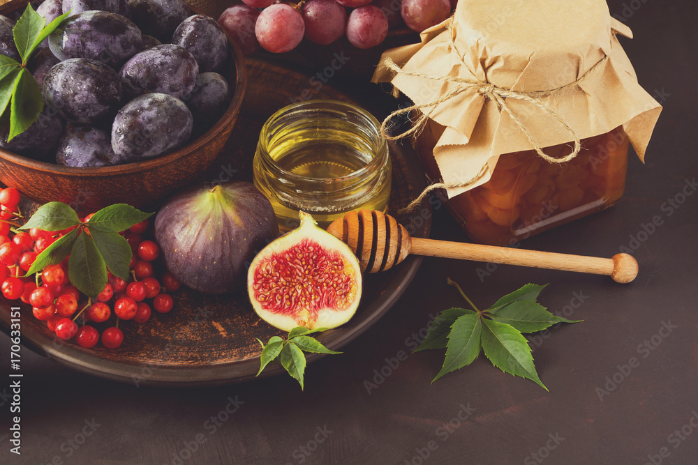 Harvest set:  plums, grapes, figs, viburnum berry, walnuts, honey and jam glasses on dark wooden desk. Still life. Toned image