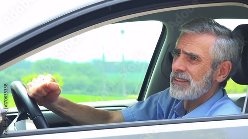 Senior man sits in the car and has depression - closeup shot from side - countryside in the background 
