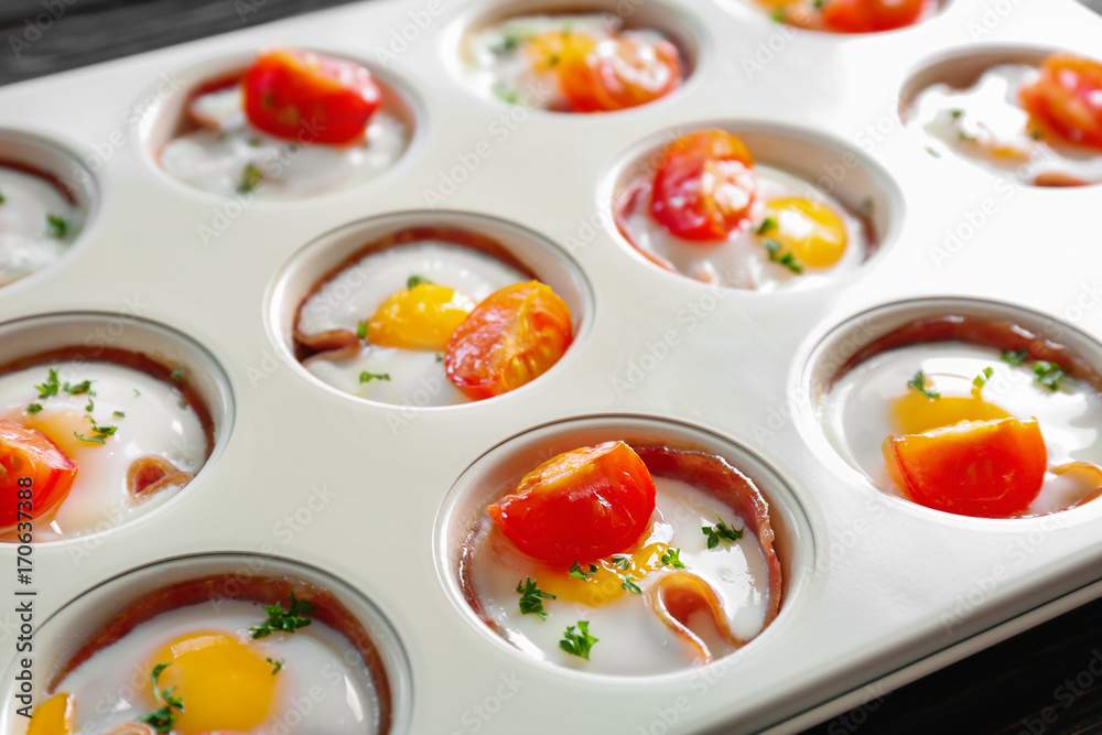 Baking mold with tasty eggs, tomatoes and ham on table, closeup Baking mold with tasty eggs, tomatoes and ham on table, closeup