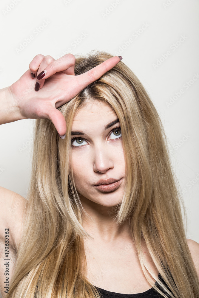 Fototapeta premium Close-up portrait of a young beautiful blonde girl on a light background. A woman with different emotions on her face.
