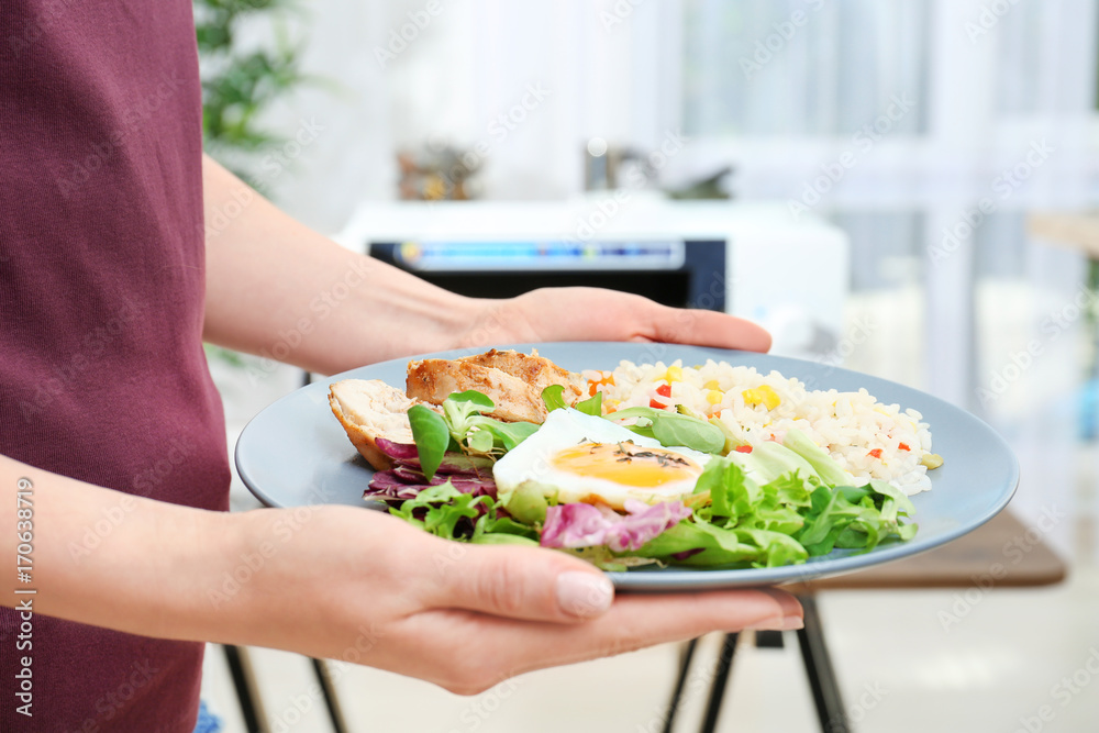 Woman holding plate with nutritious food in kitchen