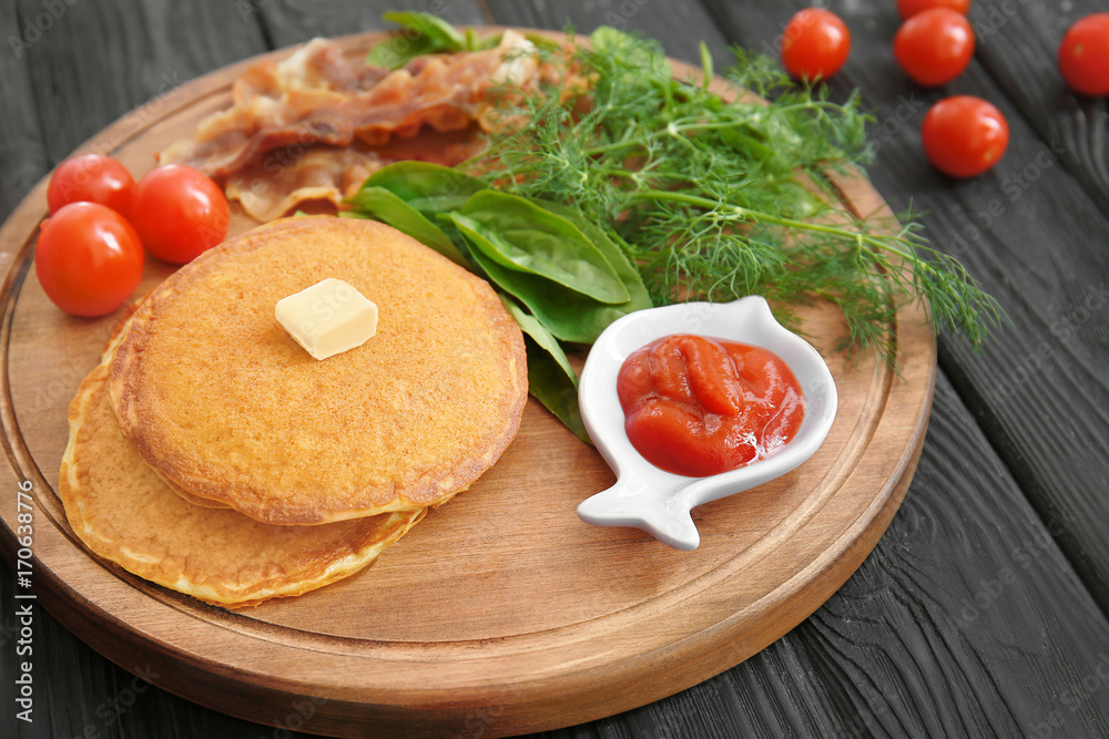 Tasty breakfast with pancakes, bacon and vegetables on wooden board