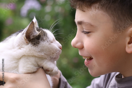 happy boy hold cat smiling close up photo on the summer green garded background photo