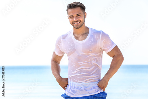 Photos Handsome young man in wet t-shirt on sea beach