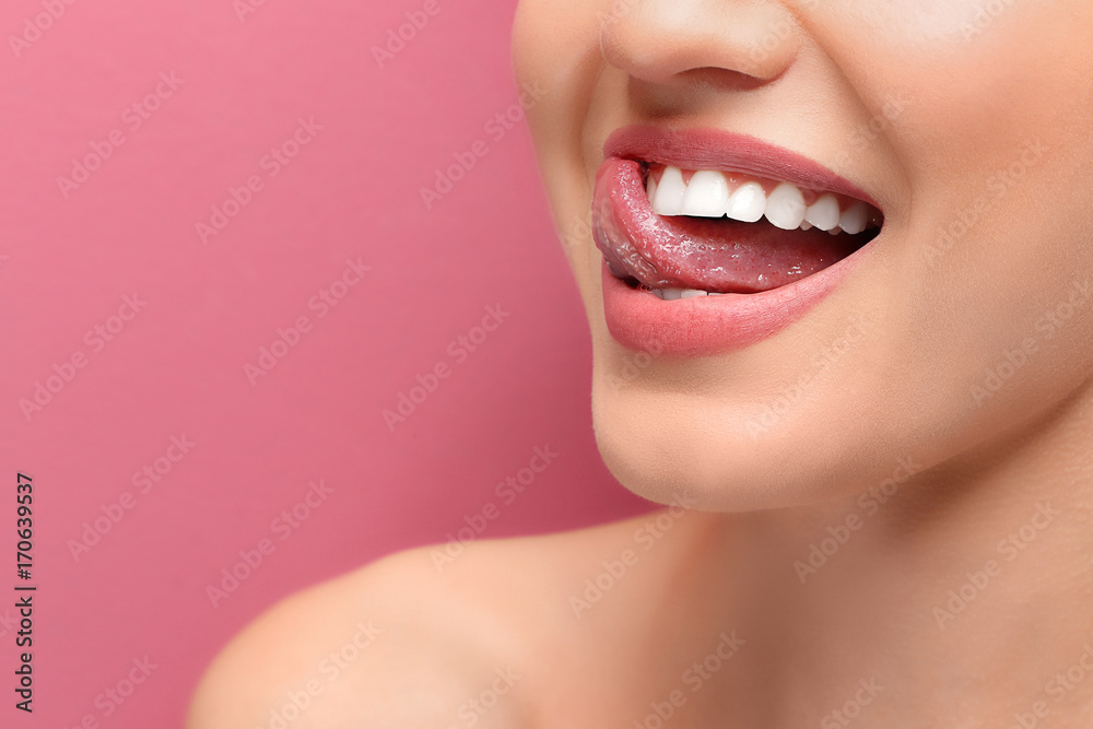 Fototapeta premium Młoda uśmiechnięta kobieta lizanie jej zębów na kolorowym tle, zbliżenie
