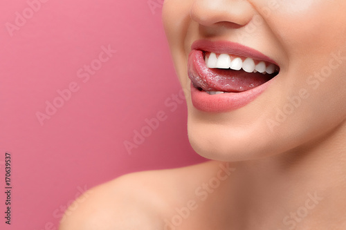 Young smiling woman licking her teeth on colour background, closeup photo