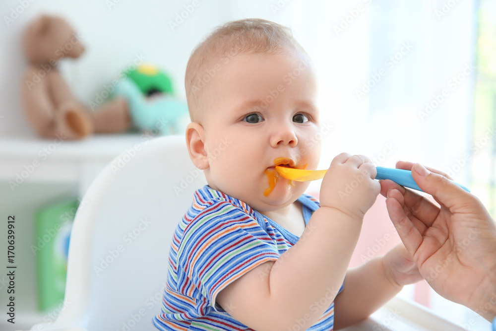 Mother feeding baby with spoon indoors Mother feeding baby with spoon indoors