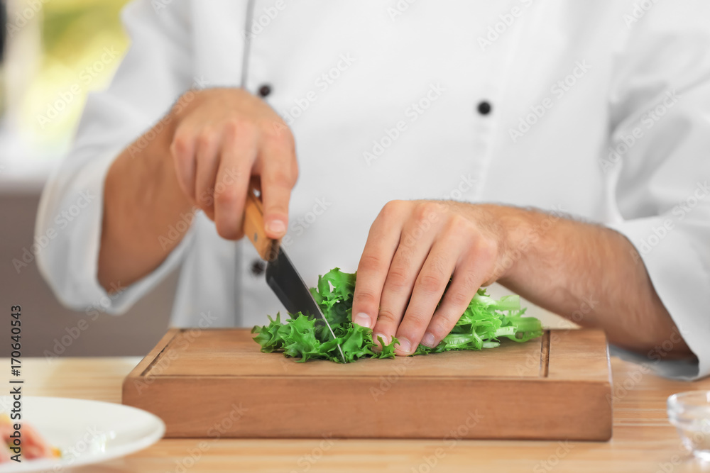 Male chef cutting salad leaves on table, closeup Male chef cutting salad leaves on table, closeup