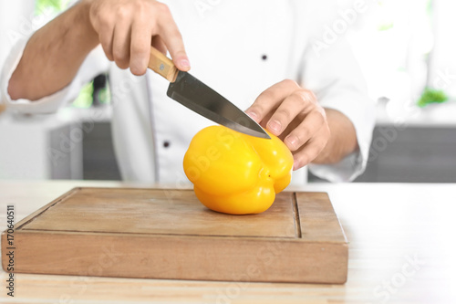 Male chef cutting paprika in kitchen, closeup