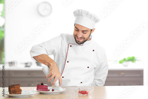 Young male chef decorating cake in kitchen
