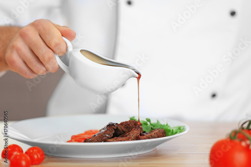 Chef pouring sauce on meat dish on table photo