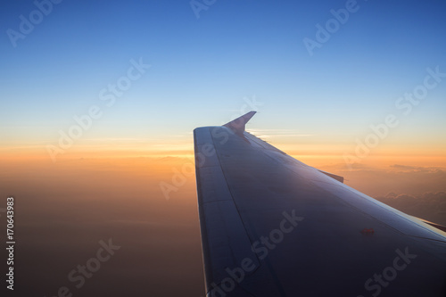 View of orangle cloudy sky and airplane wing at sunrise. Copy space.