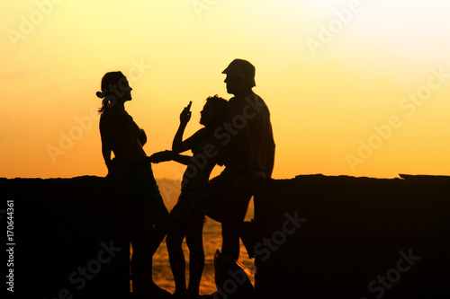 Silhouettes of young group of people sitting during sunset and take a selfie with smartphone. Hipster best friends having fun on low cost road trip. Brazil