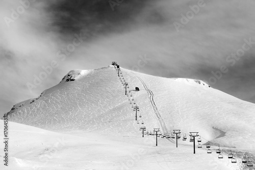 Schilderij op canvas Black and white view on ski slope and chair-lift at sun winter morning