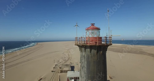 Aerial view drone video of Pelican Point Lodge and Paratus lighthouse on sand beach peninsula, Walvis Bay harbour and lagoon with ocean background with ships at Namibia's Atlantic west coast