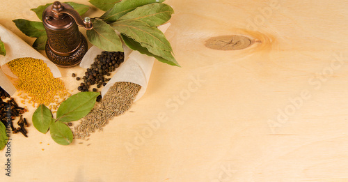 Vintage bronze mill for seasoning, various spices and branches of bay leaf on a wooden background with space for designer text.