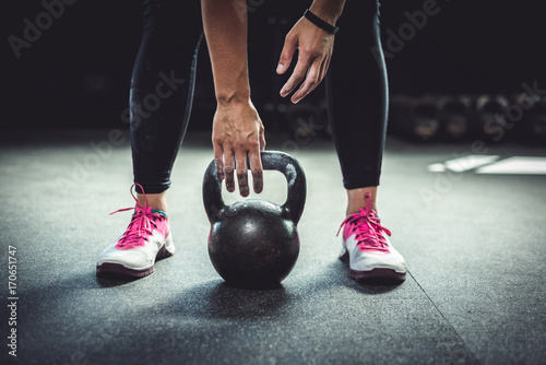 Woman in gym reaching for a kettlebell, with chalked hands. Authentic mood.