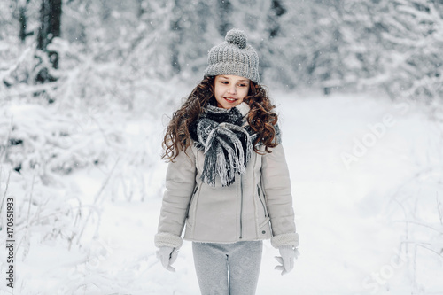 Little girl in winter forest in fur hat with pompon.