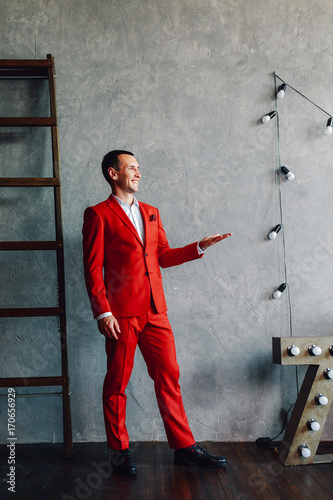 Studio portrait of a happy modern man in a white shirt and red suit against a gray background.