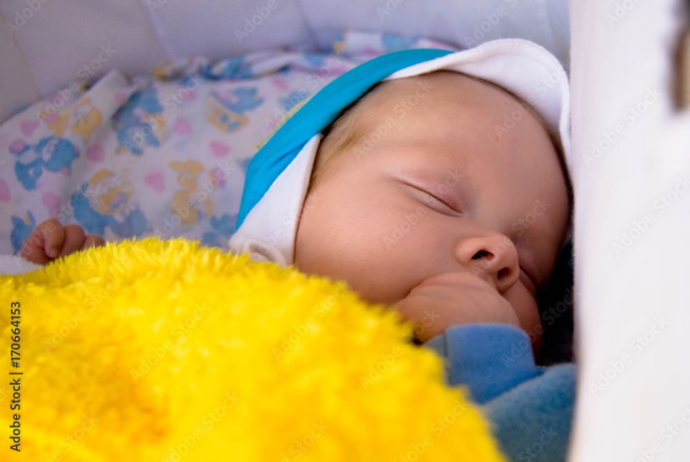 Portrait of sweet sleeping newborn baby in cap under yellow blanket