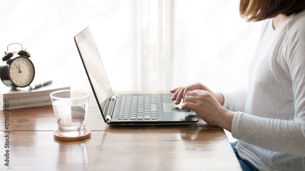 Naklejka premium Woman hands typing on laptop keyboard on wooden table at home