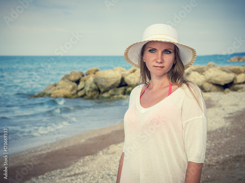 Beautiful woman in white hat on a background of large stones on the beach.