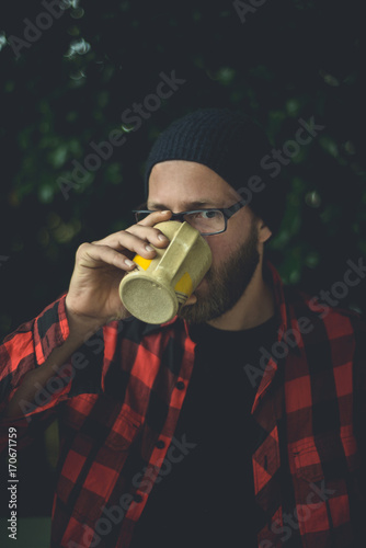 Happy hipster sipping a cup of coffee on his porch in the morning in a natural setting. photo