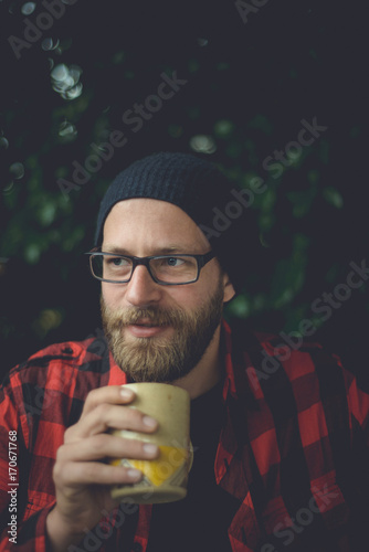 Happy hipster sipping a cup of coffee on his porch in the morning in a natural setting. photo