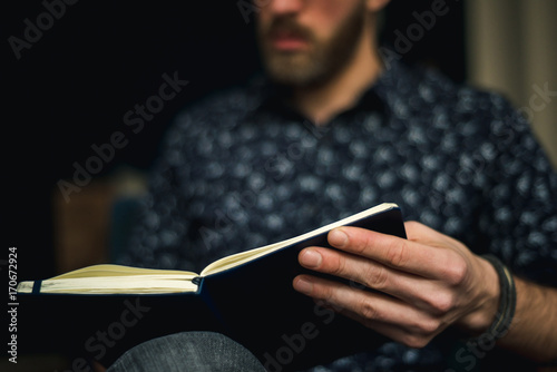 Foto Man is sitting and reading a book at home.